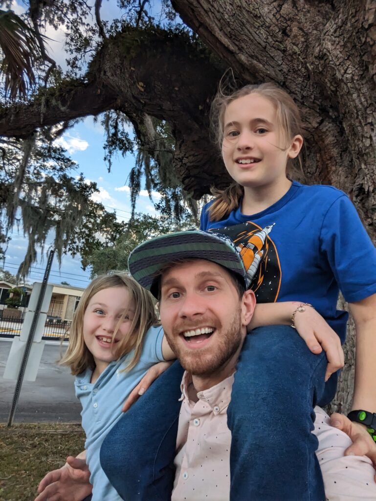 family posing for a photo outdoors near a large tree